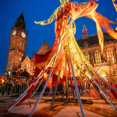 Large figurative sculpture made of metal and fabric in front of the town hall at dusk lit with warm lighting