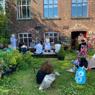 Ebor Studio: Group of people sat on the ground and benches in a summer garden listening to a man talk about bees