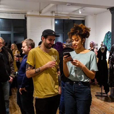 Ebor Studio: room of people chatting with drinks in white spot lit room with rails of clothing