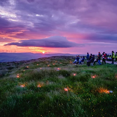 Breaking Barriers: Group of people sit watching the sun set over the moors