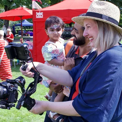 Breaking Barriers: Baby wates a woman in blue top and straw hat operate a camera in a sunny park